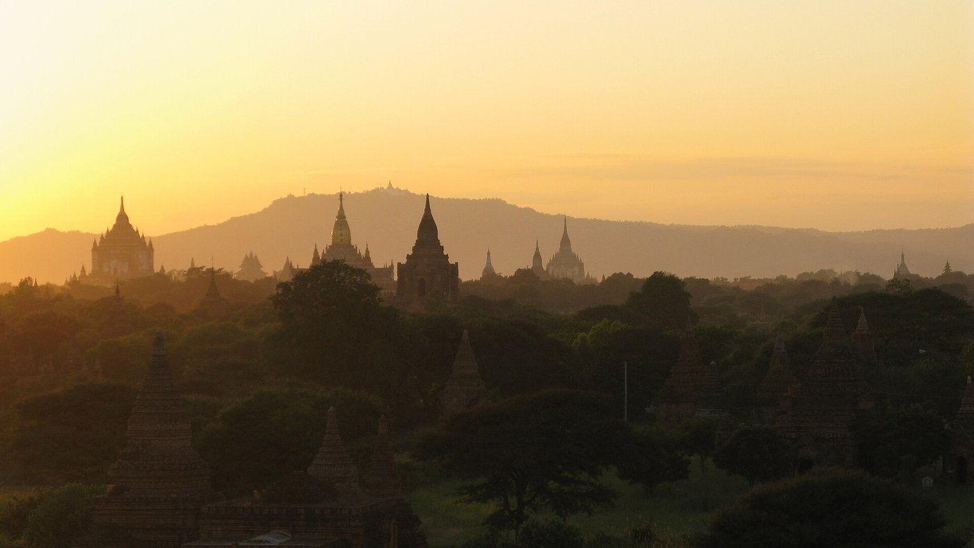 The plain of Bagan at sunset, hundreds of brick temples and stupas spread across the dry landscape under a low golden sky