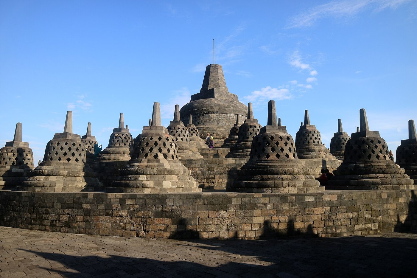 The upper circular terraces of Borobudur, lined with rows of bell-shaped perforated stone stupas under a bright sky