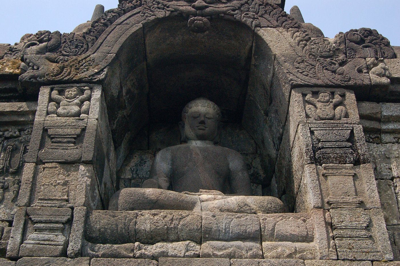 A seated stone Buddha statue glimpsed through the diamond-shaped openings of a perforated stupa at Borobudur