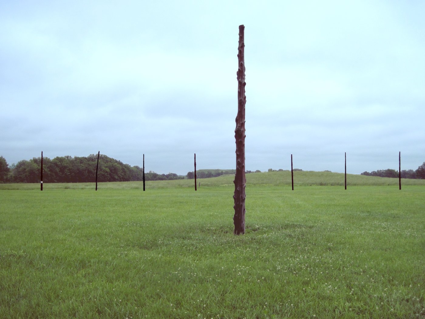 Reconstructed Woodhenge at Cahokia at sunrise, a ring of tall wooden posts silhouetted against an orange sky