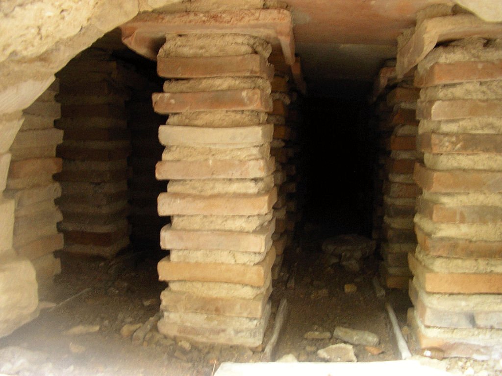 The hypocaust underfloor heating system at Great Witcombe Roman villa in Gloucestershire, showing rows of brick pillars beneath a raised floor