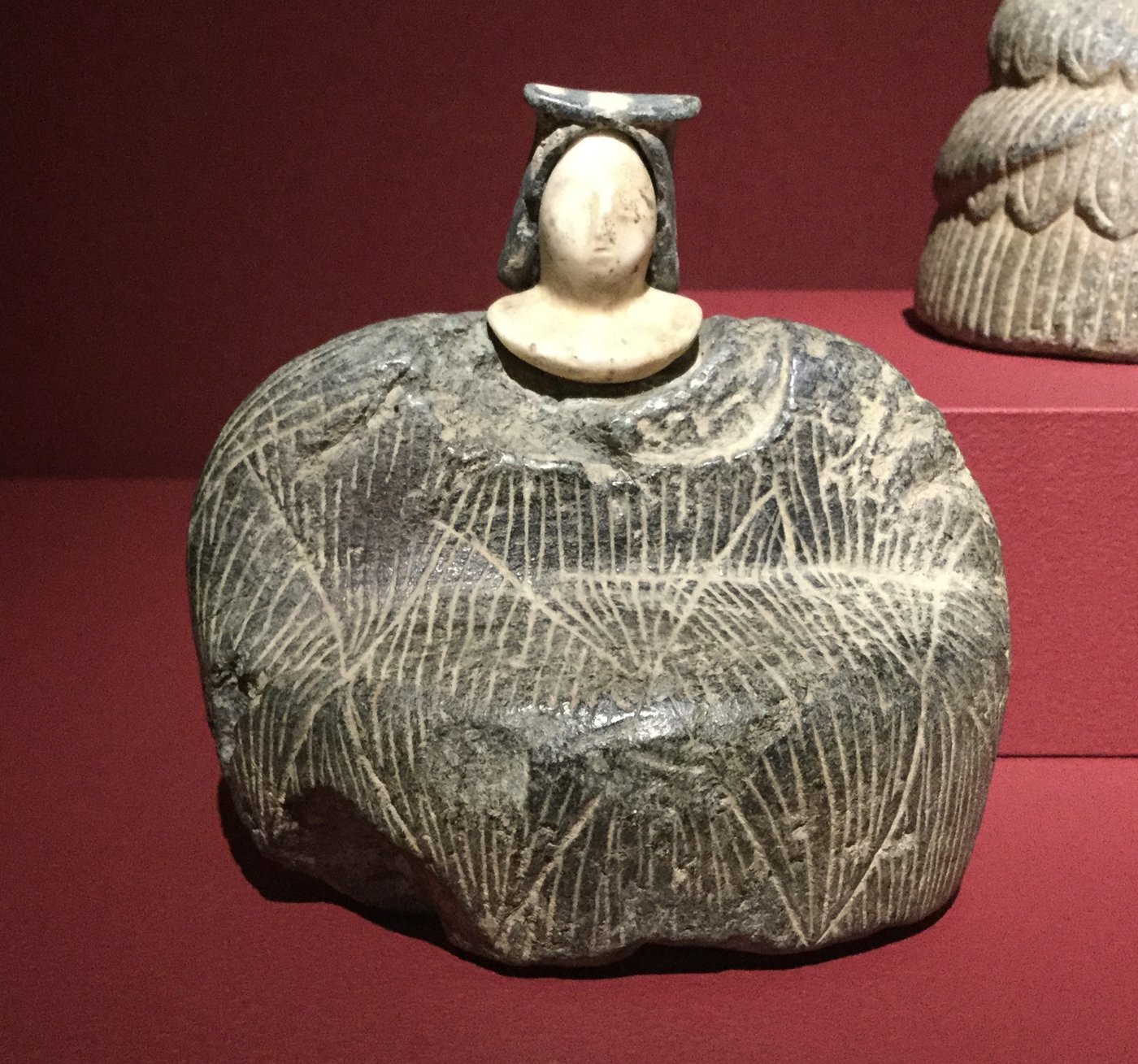 A Bronze Age Bactrian composite female statuette with a pale stone head and dark chlorite robe carved as fleece