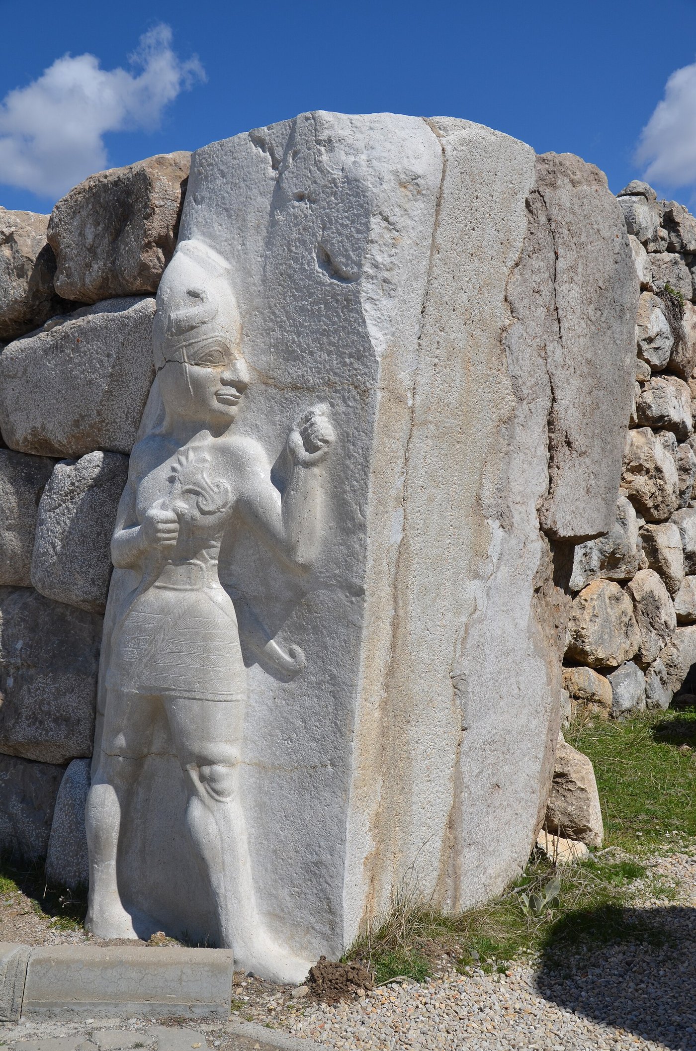 A carved relief of a striding figure in a horned helmet and kilt with an axe over his shoulder, cut into a large stone block at the King's Gate of Hattusa