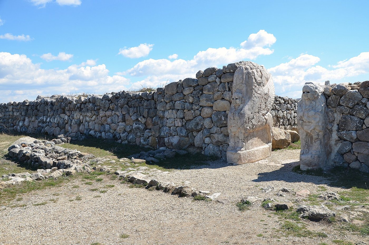 Weathered stone bases of the Sphinx Gate on a green ridge at Hattusa, under a wide sky