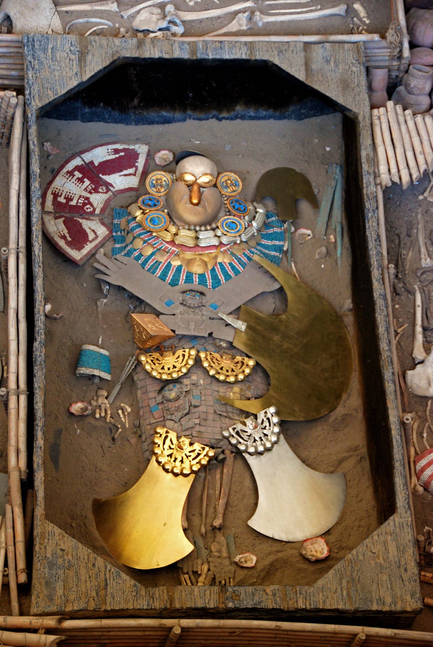 The excavated regalia of the Lord of Sipán laid out as found: a gilded face with gold eyes and nose, turquoise bead collars, and matching gold and silver crescent ornaments