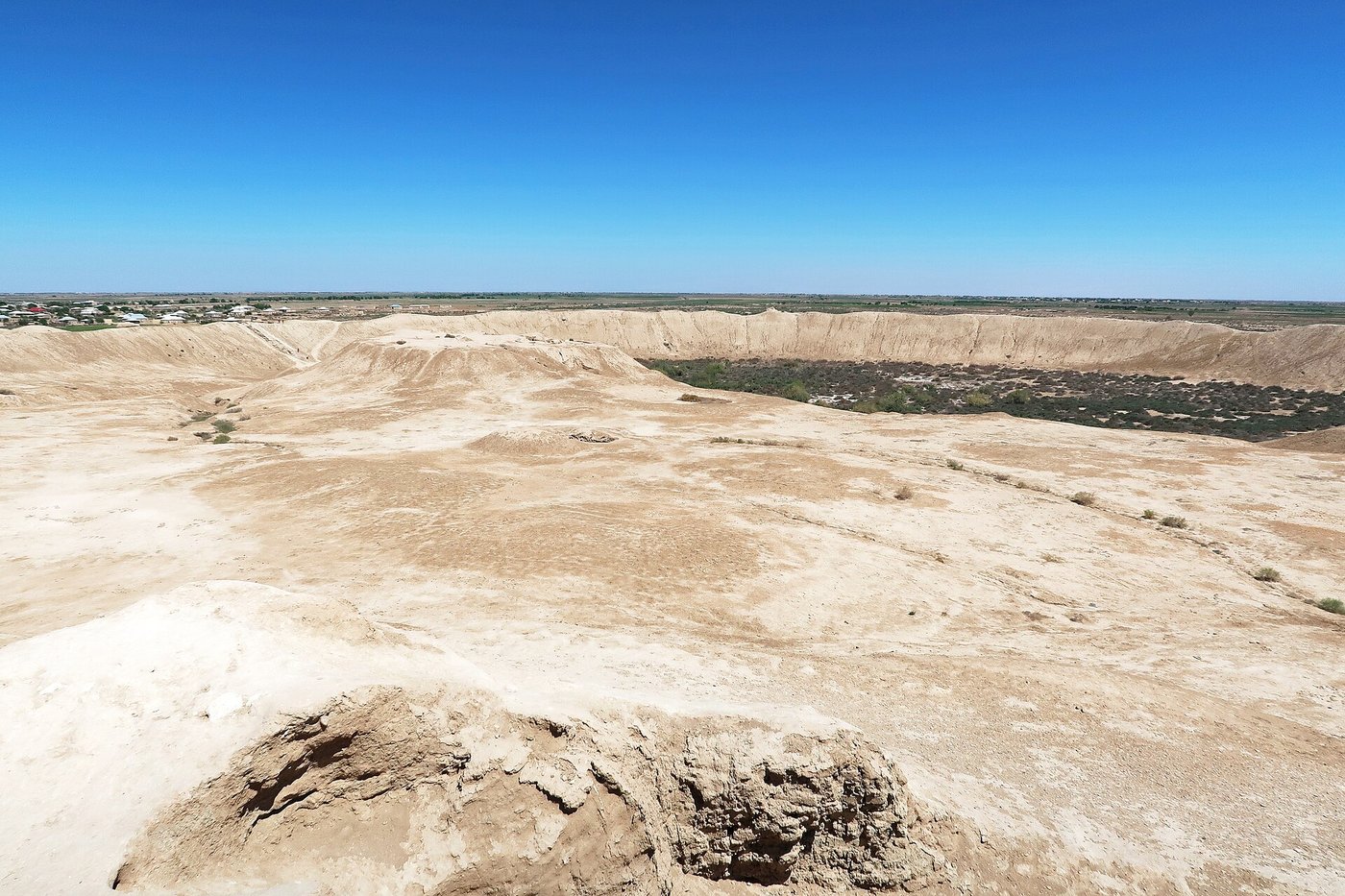 The eroded earthen ramparts of Erk Kala, the oldest walled city at Merv, rising as a grassy mound against a bright sky