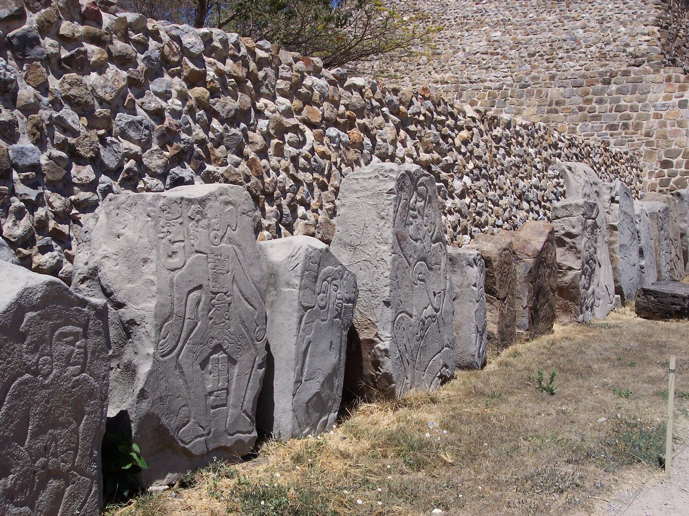 A single danzante slab, the carved figure sprawled with closed eyes and an open mouth, small glyph signs beside the head