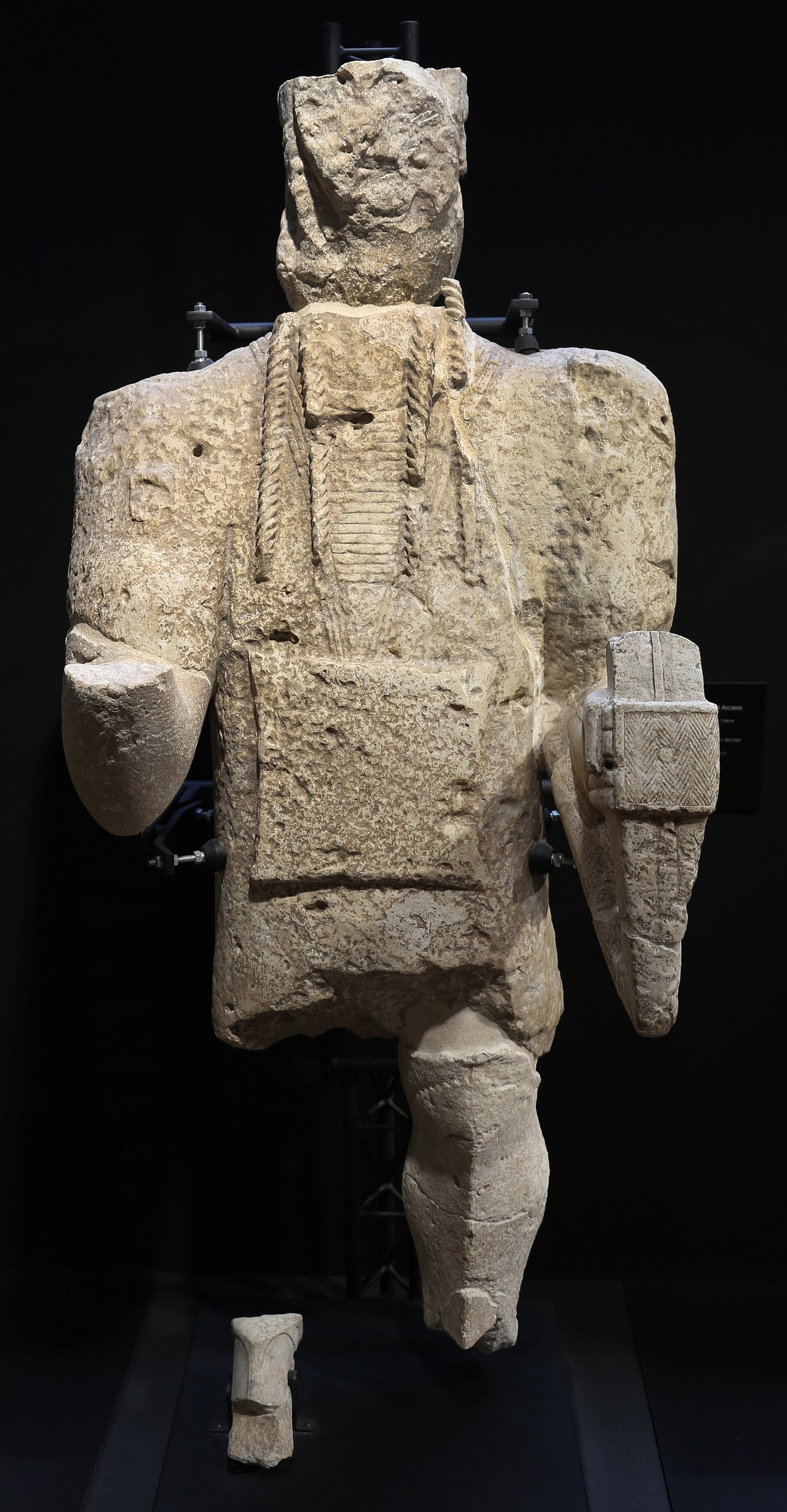 A reassembled Mont'e Prama archer statue in pale sandstone, standing over two metres tall, with a bow held across the chest and the characteristic circular eyes
