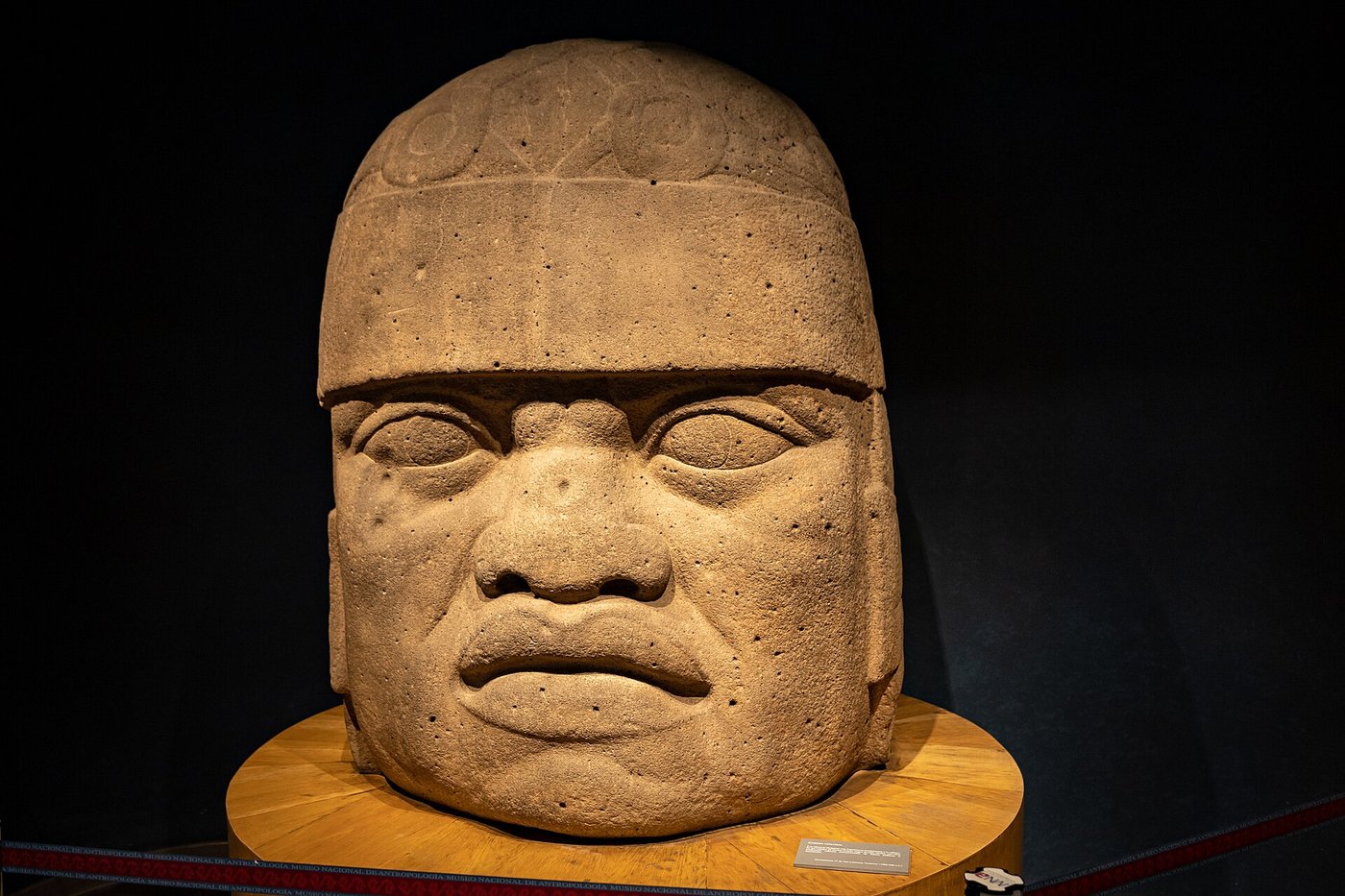 Close view of the deep-set eyes, broad nose and helmet band of a colossal Olmec head, showing the polished basalt surface.
