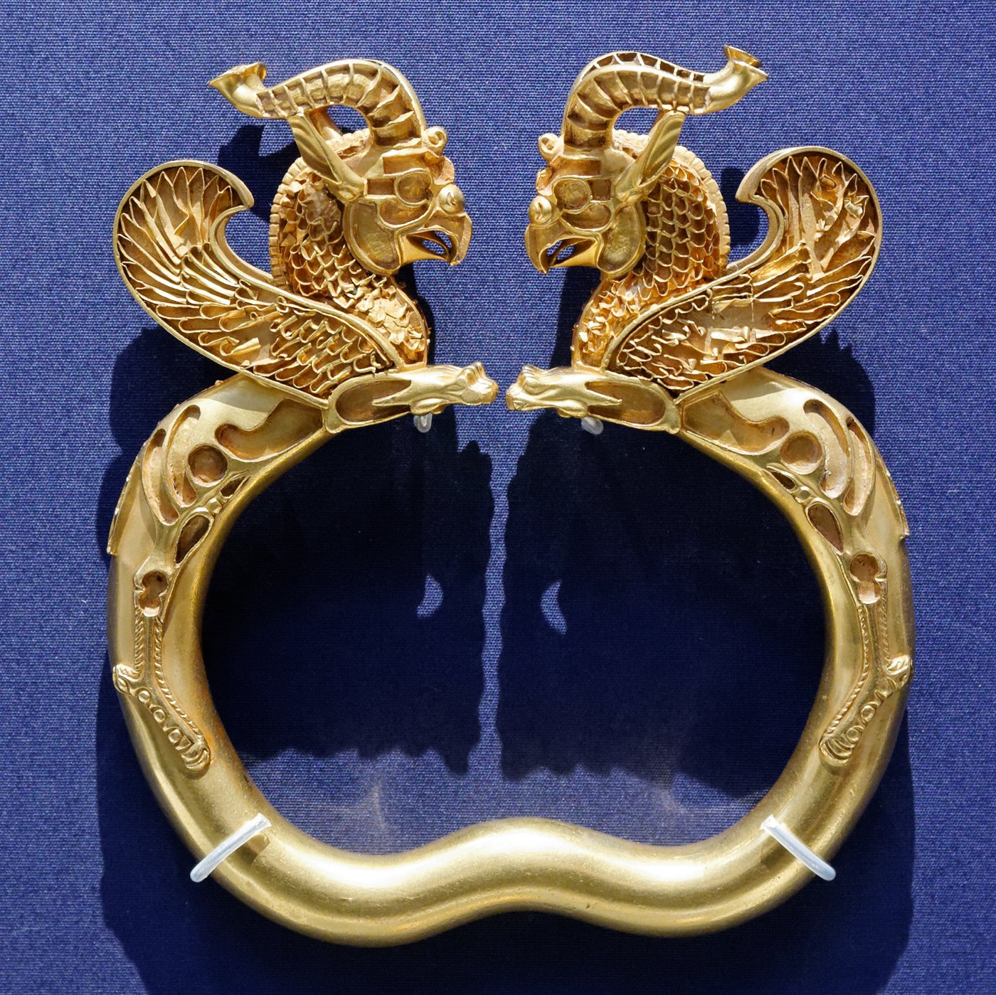 Gold armlet with two winged griffin heads facing each other, the sockets once set with coloured inlay