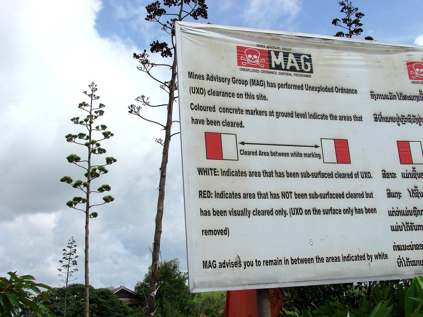 A red-and-white sign warning of unexploded ordnance beside a walking path at the Plain of Jars