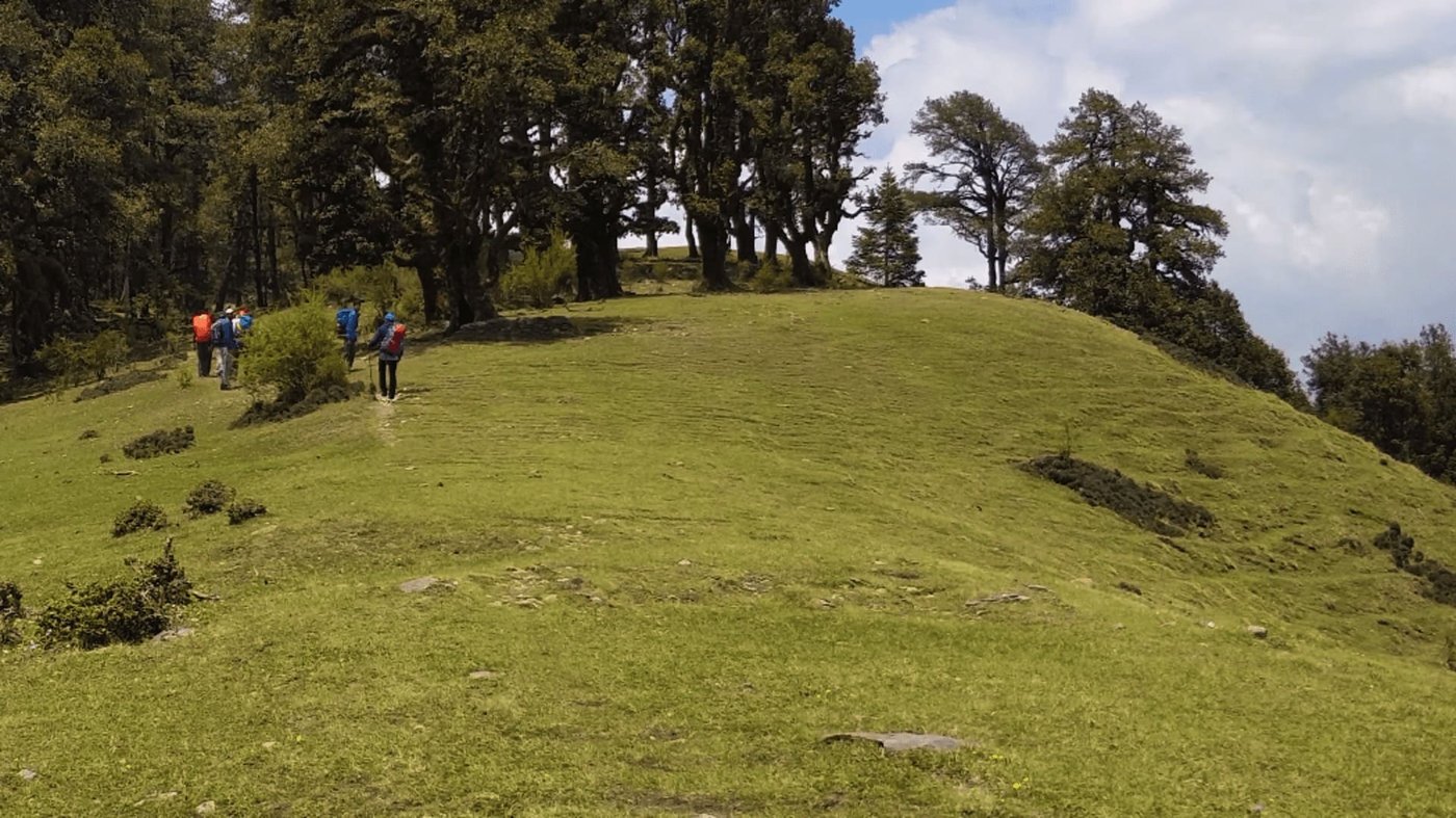 Trekkers following the grassy ridge route toward the Roopkund basin in the Himalayas
