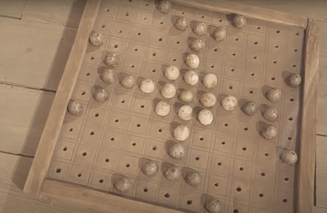 A wooden hnefatafl gaming board set up mid-game with pale bone playing pieces, a single king piece at the centre