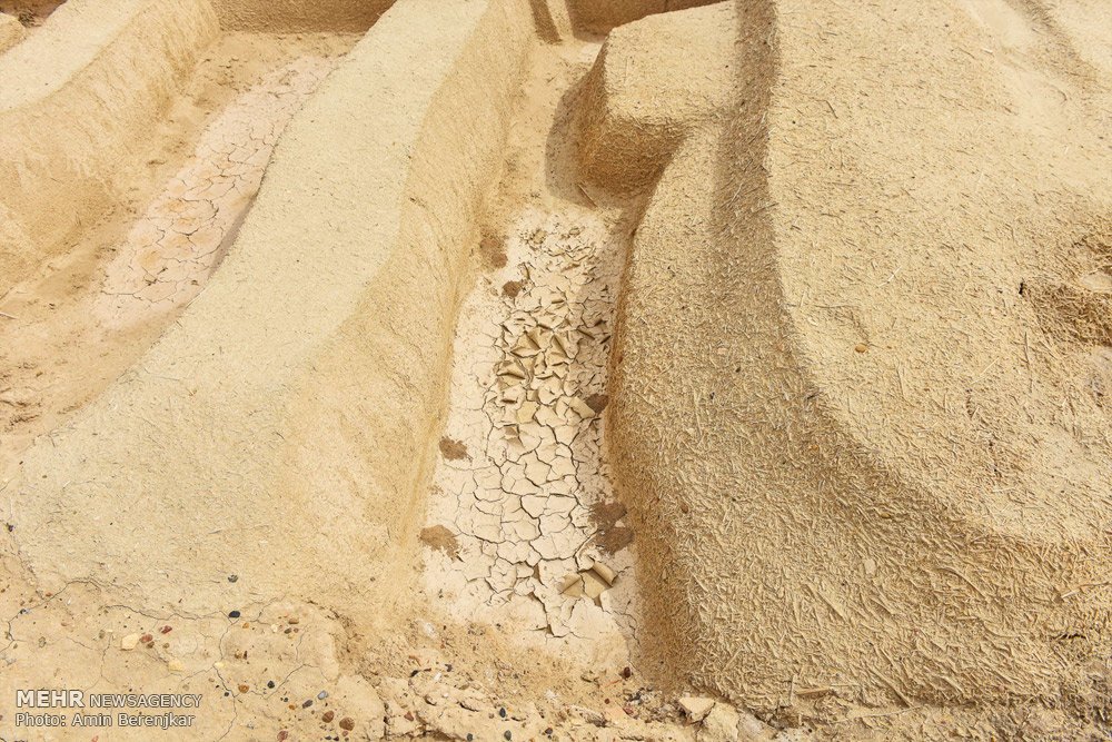 Eroded mudbrick walls and low mounds of the Burnt City under a pale desert sky.