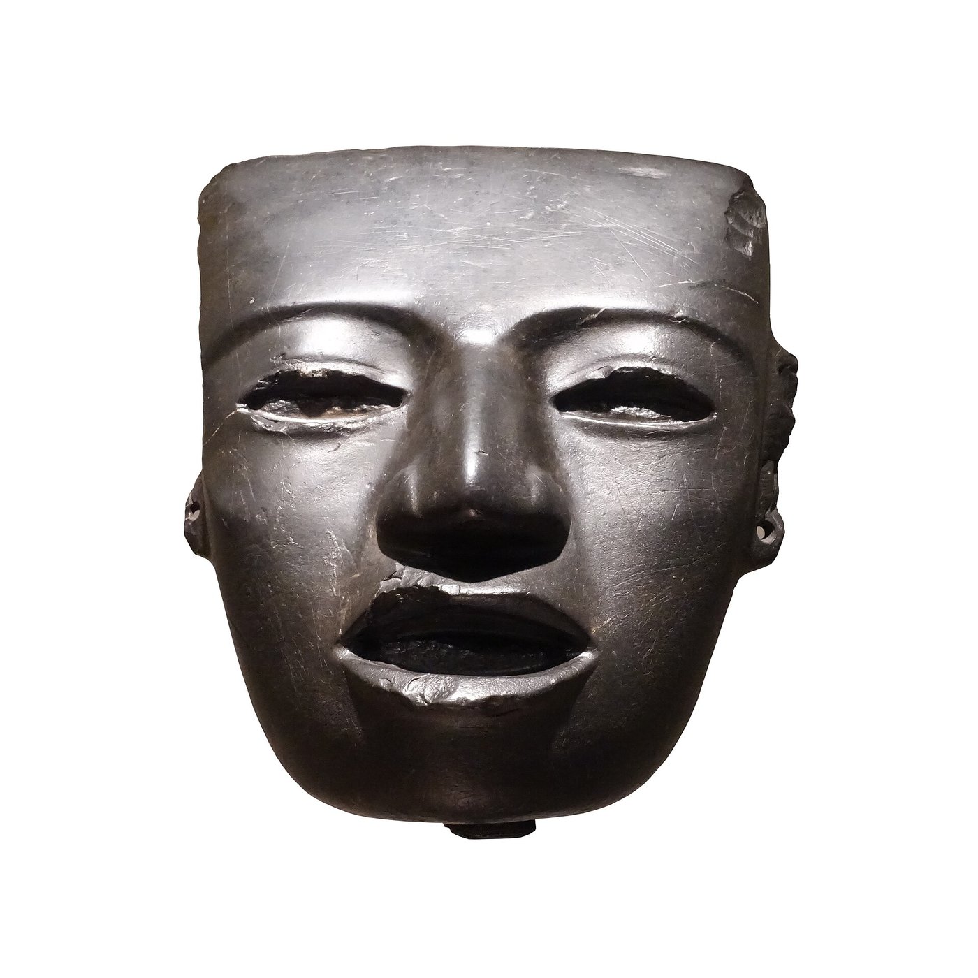 A pale greenstone Teotihuacan mask with a broad calm face, hollow eyes and slightly parted lips, on a dark background.
