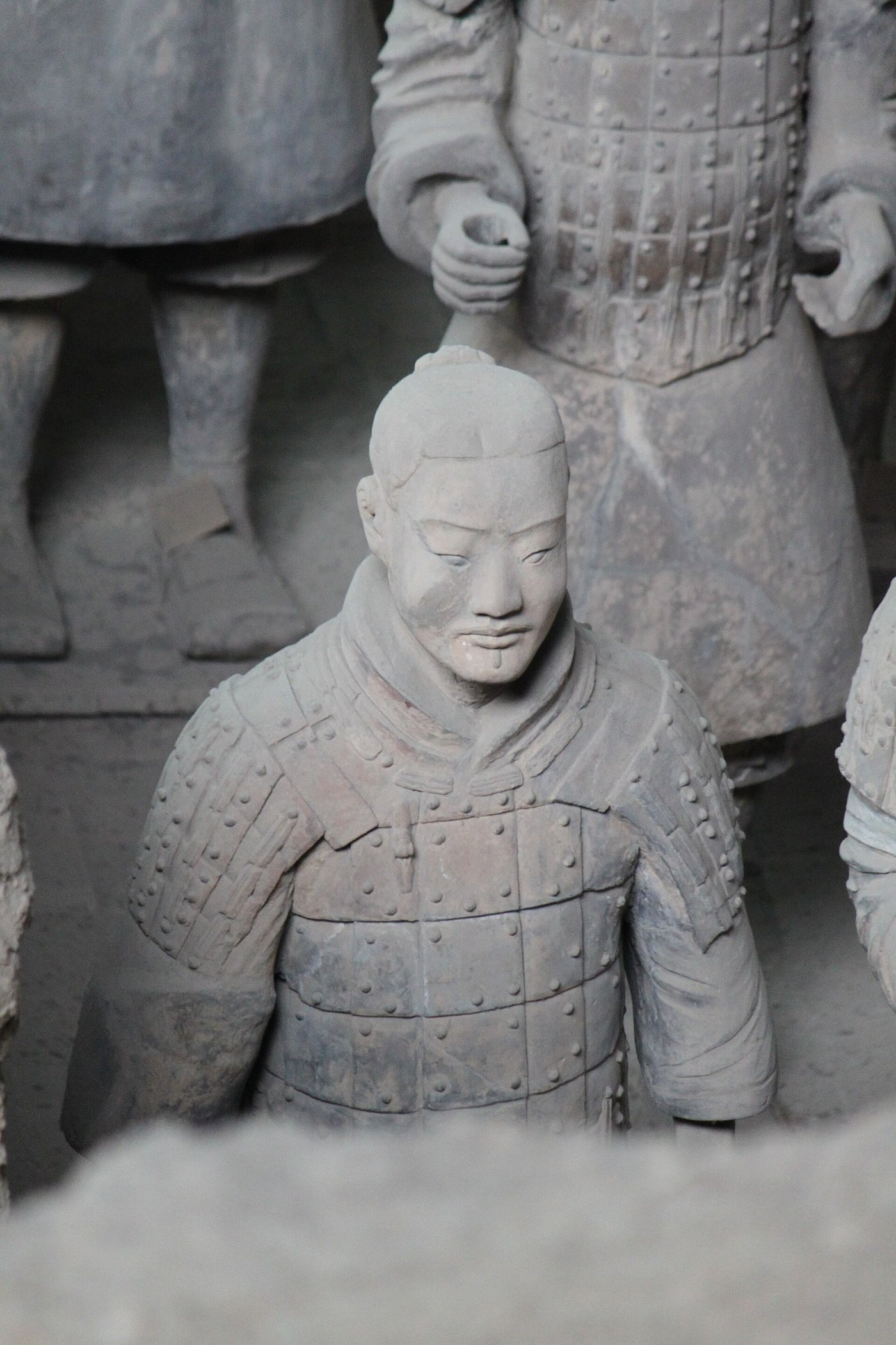 A single terracotta infantryman in plated armour with a topknot, standing among other warriors in the excavation pit