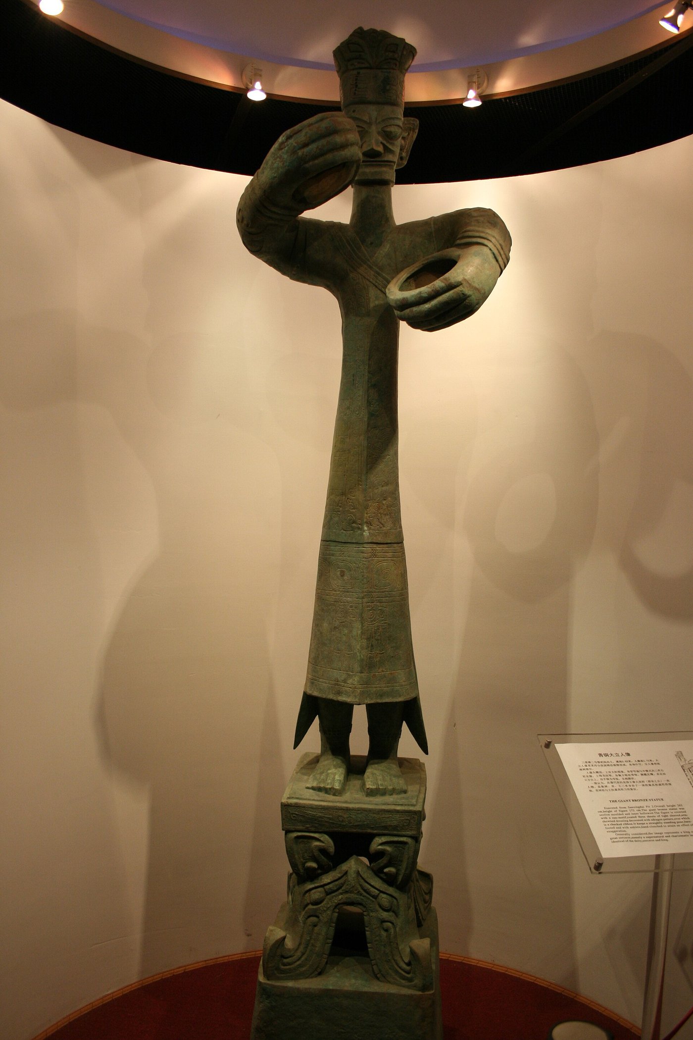 The tall bronze standing figure from Sanxingdui, on a decorated base with oversized hands
