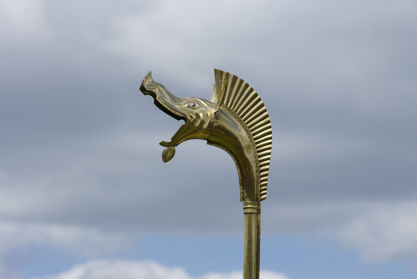 A performer standing and playing a reconstructed carnyx, the long bronze tube rising vertically past his face to a boar's head high above