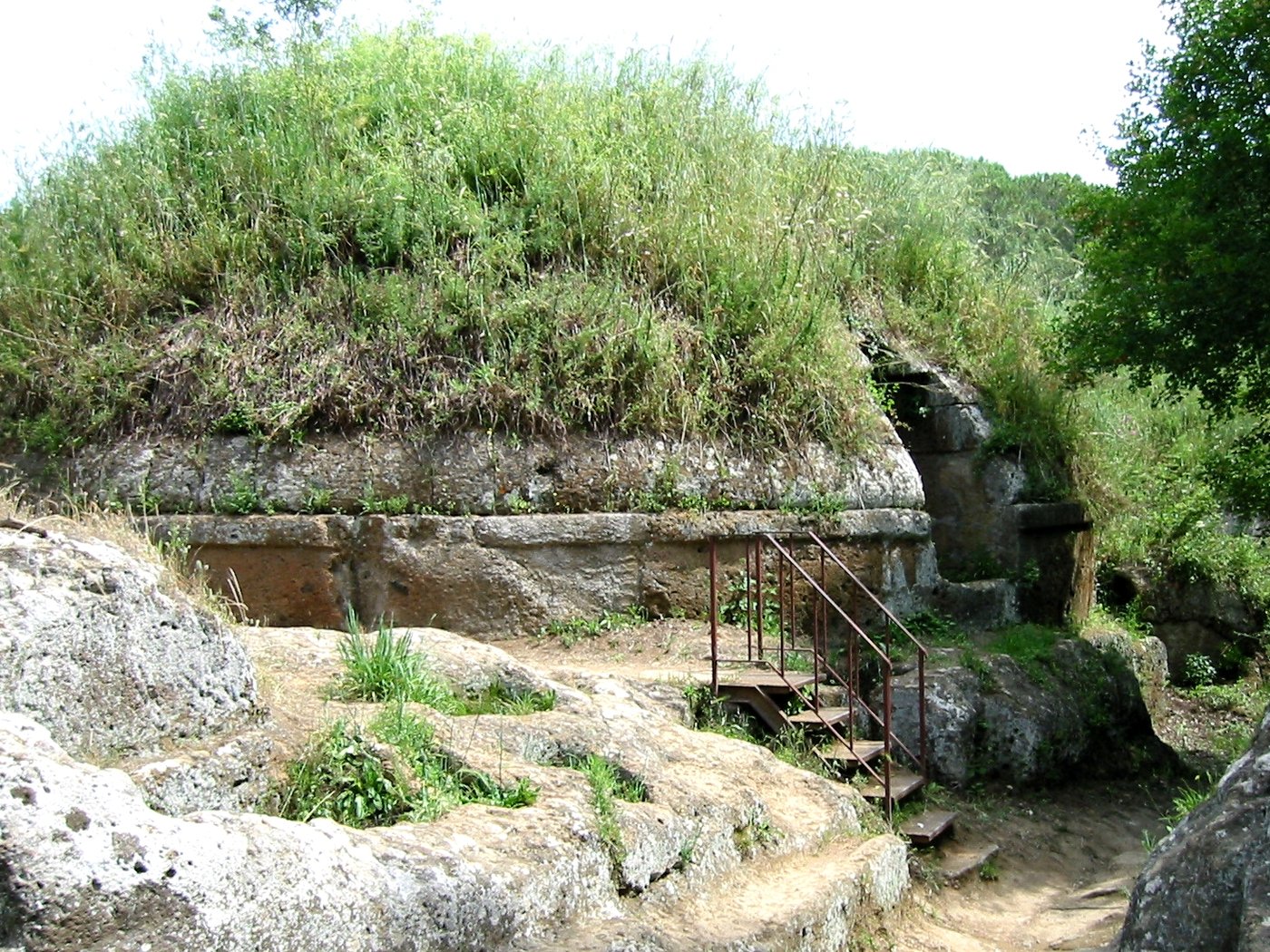 Grass-covered circular burial mound with a carved stone base at the Banditaccia necropolis in Cerveteri, Italy