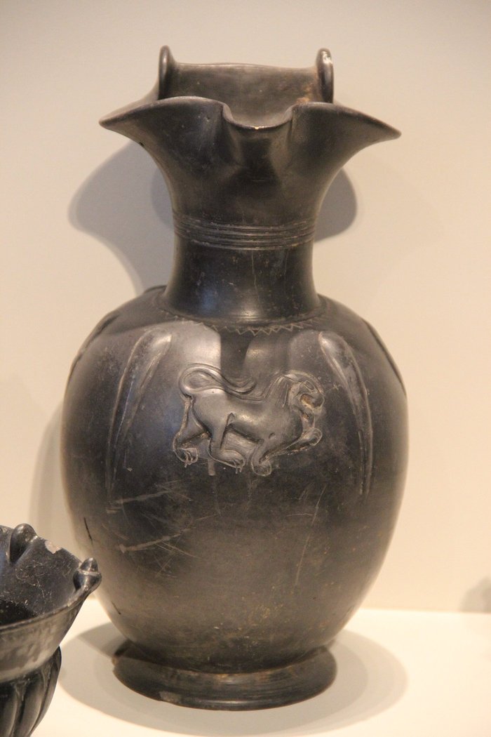 Glossy black Etruscan bucchero jug with a trefoil mouth and a small horse in relief on its body
