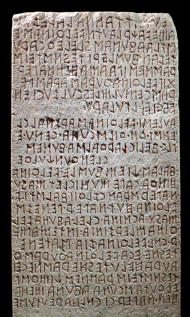 Tall stone slab covered in dozens of lines of incised Etruscan lettering, the Cippus Perusinus from Perugia