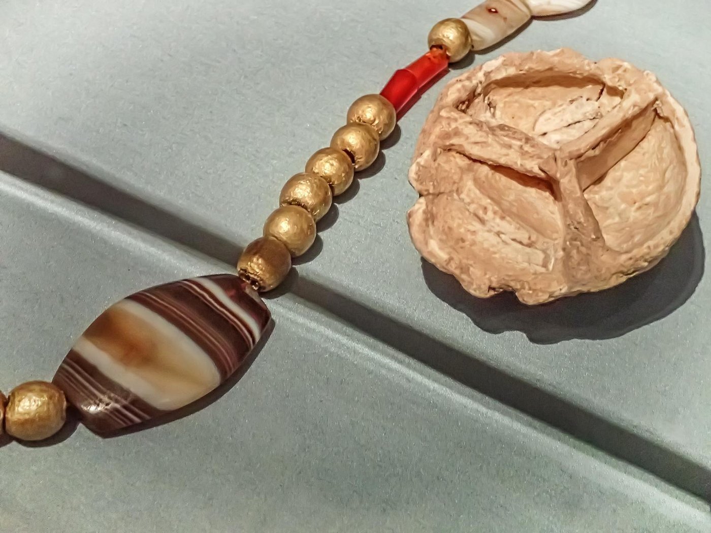 A necklace of gold, banded agate and carnelian beads with a fluted gold cosmetics container, from the Royal Cemetery of Ur
