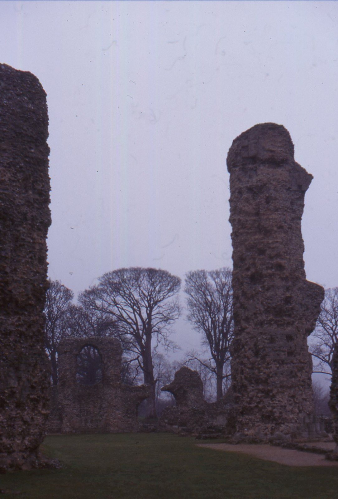Tall stone ruins of Bury St Edmunds Abbey rising against the sky, with green lawn in the foreground