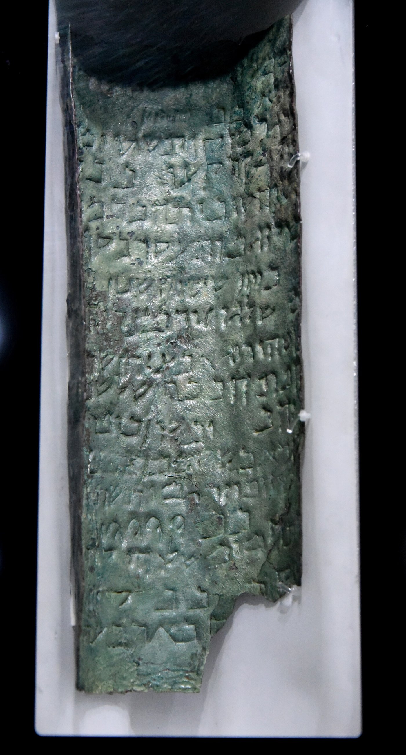 A curved strip of the Copper Scroll showing rows of punched Hebrew letters