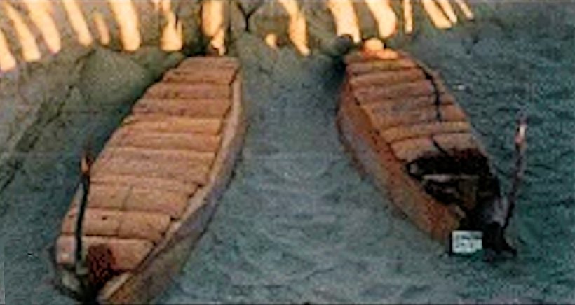 Boat-shaped wooden coffins from the Xiaohe cemetery in the Tarim Basin, surrounded by tall wooden posts in the sand