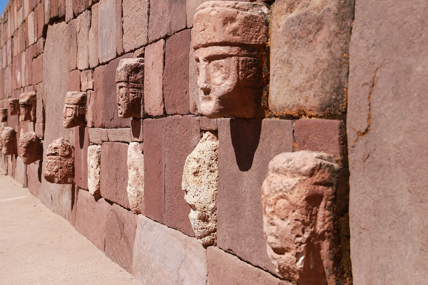 Stone faces of many different styles set into the walls of a sunken rectangular courtyard at Tiwanaku