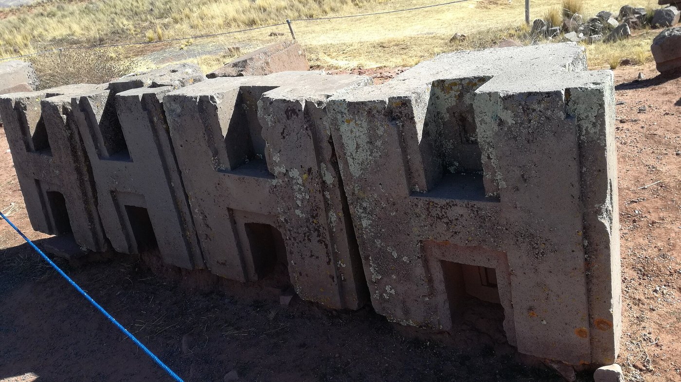 Precisely cut grey stone blocks lying scattered at Pumapunku, with sharp right-angled edges and flat faces