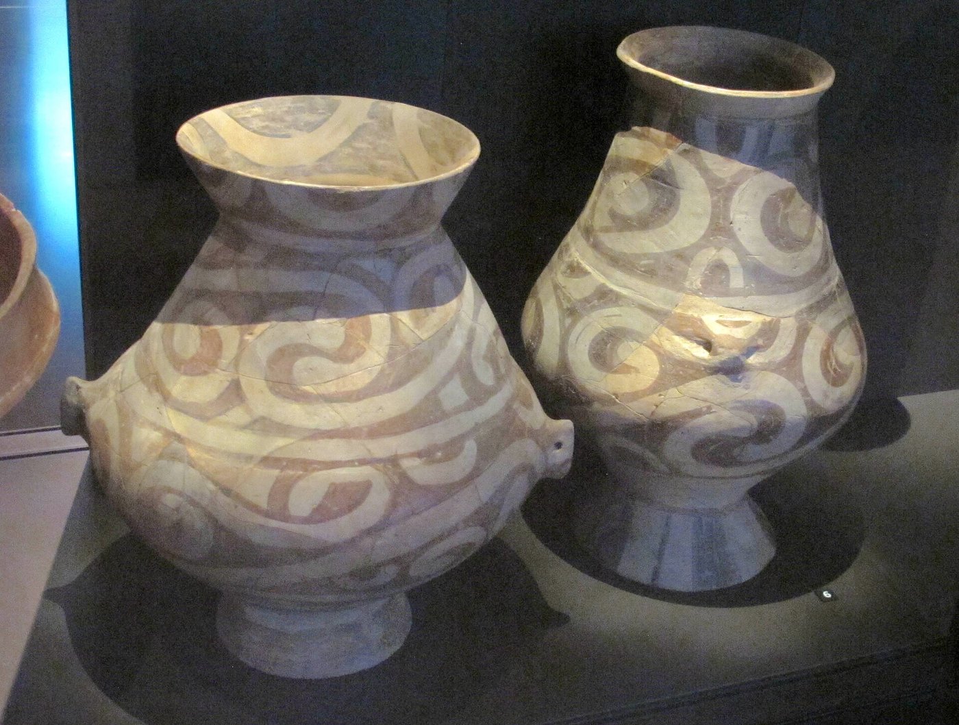 Two tall Cucuteni-Trypillia painted ceramic jars decorated with red, white and dark swirling spiral patterns, in a museum display