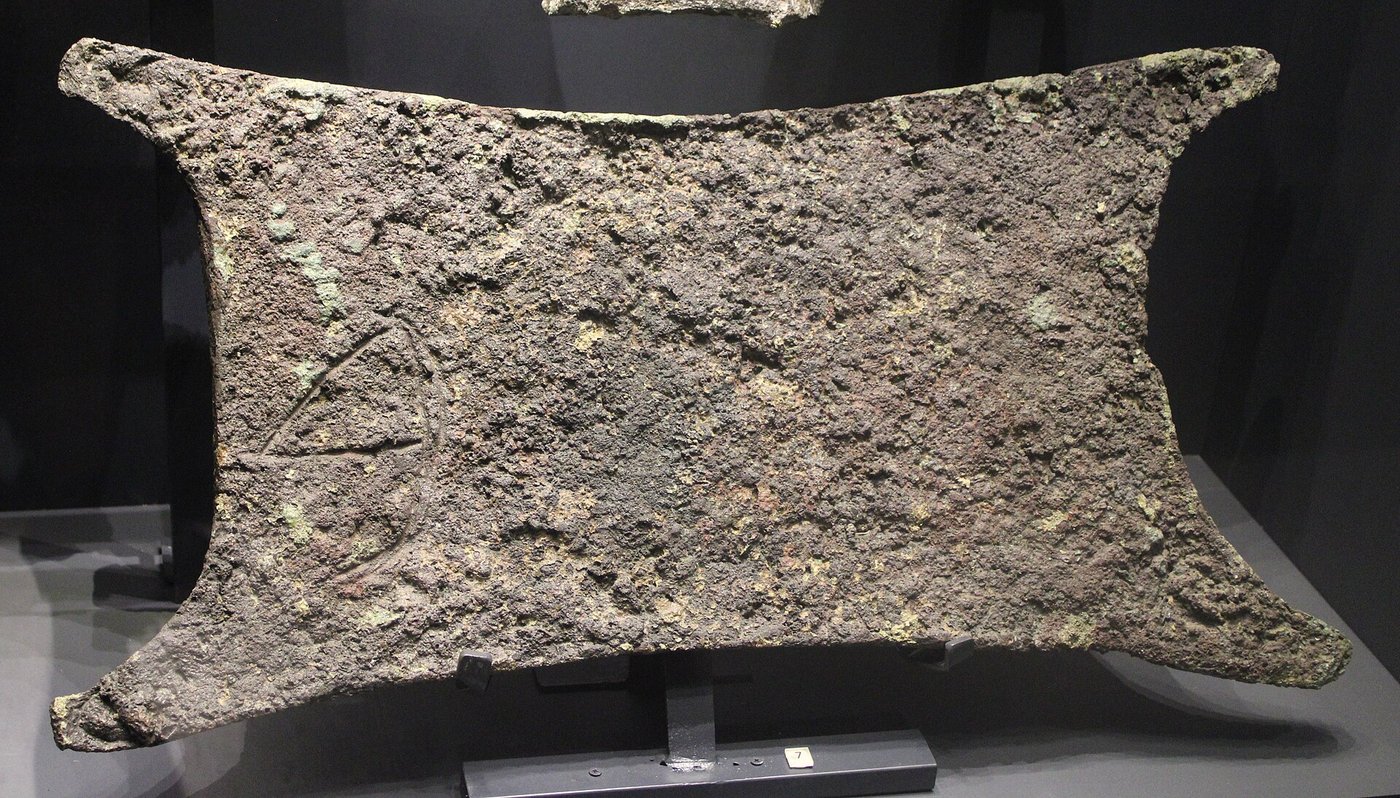 A corroded copper oxhide ingot from the Uluburun shipwreck, a flat slab with a handle-like projection at each corner