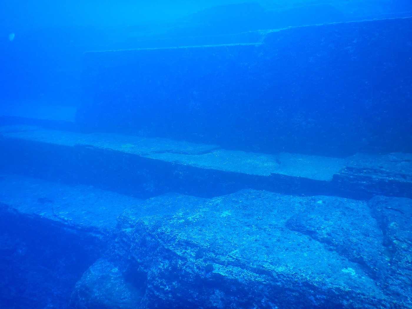 Wide underwater view of the terraced stone mass at Yonaguni, flat platforms stepping down through green water