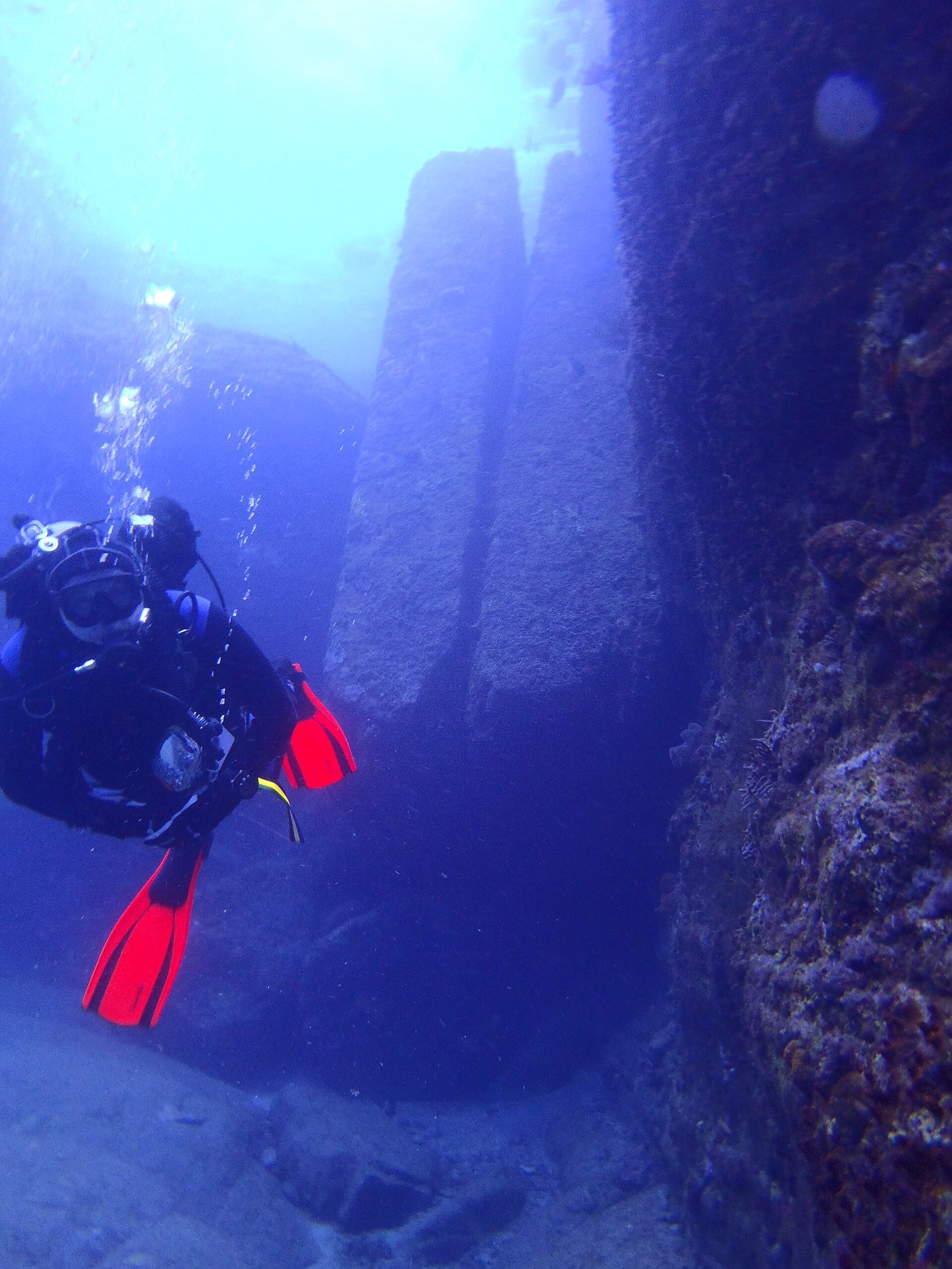 Two tall parallel stone pillars standing close together at the Yonaguni Monument, divers nearby for scale
