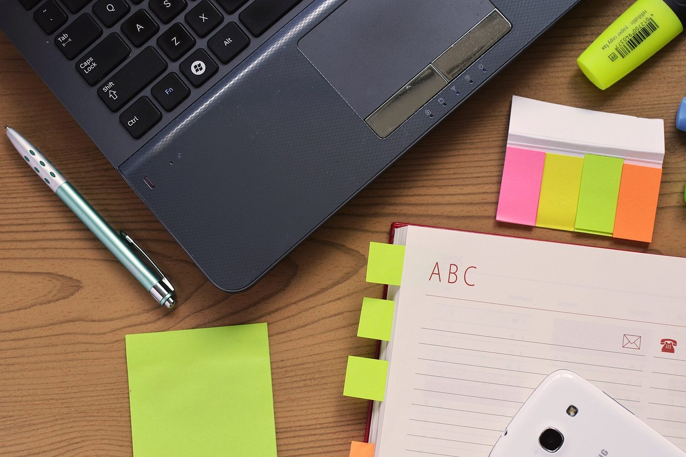 A desk with a laptop, notebook, pen and sticky notes