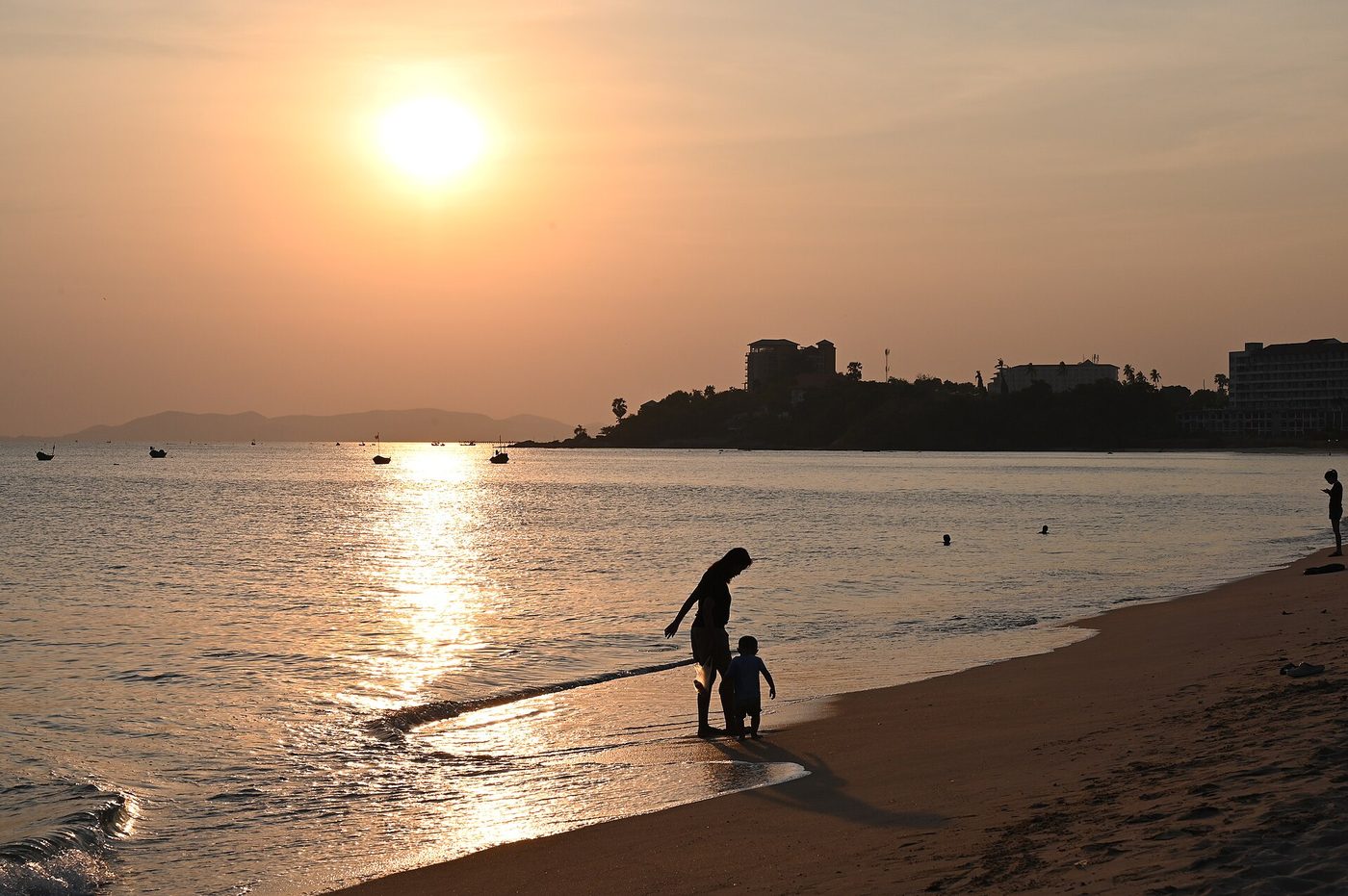 A parent and child walking along a beach at sunset